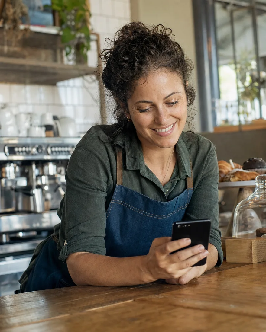 A café owner smiling at her phone behind the counter